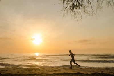 Silhouette man run on beach with sunrise and sea background