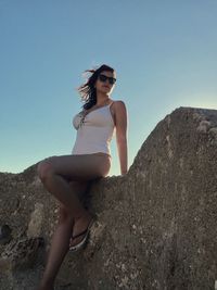 Portrait of young woman on rock against clear sky