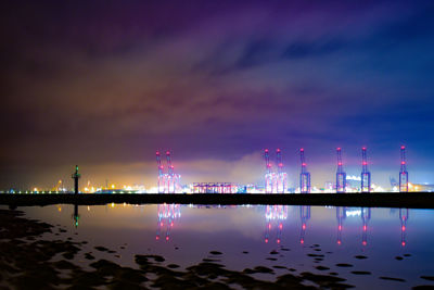 Illuminated bridge over river against sky at night