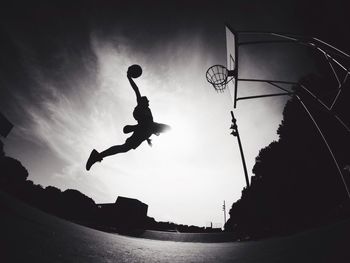 Low angle view of man in mid-air putting ball in basketball hoop