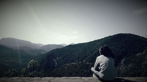 Rear view of woman sitting on mountain against clear sky