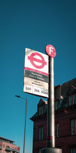 Low angle view of road sign by building against clear blue sky