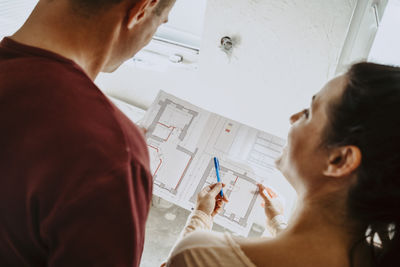 Rear view of couple discussing over floor plan while renovating home