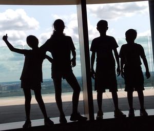 Silhouette people standing against sky seen through window