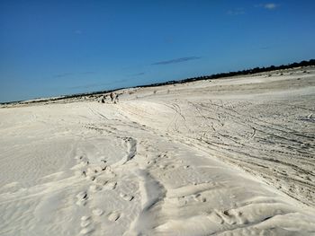 Tire tracks on sand dunes against clear blue sky