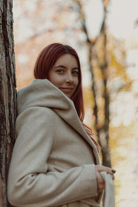 Portrait of smiling woman standing by tree trunk