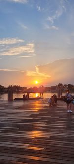 People on pier against sky during sunset