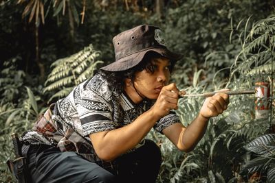 Young man wearing hat holding toy against plants in forest