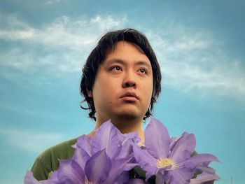 Portrait of young man with purple clematis flowers against blue sky.