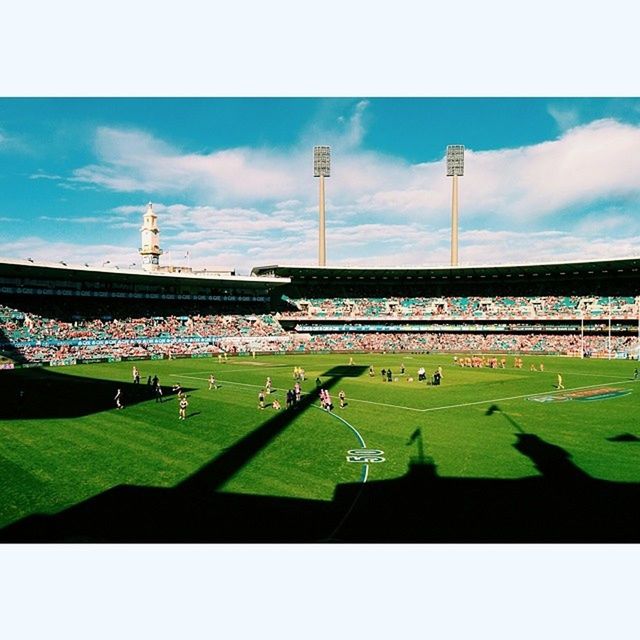 grass, transfer print, sky, green color, building exterior, architecture, built structure, large group of people, field, auto post production filter, cloud - sky, grassy, cloud, outdoors, day, sport, lawn, stadium, landscape, blue