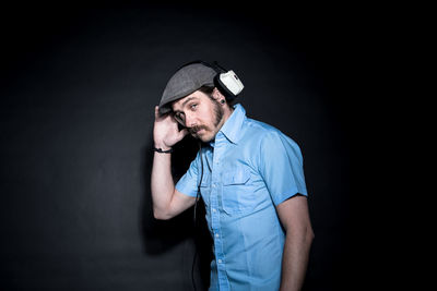 Portrait of confident man with headphones standing against black background