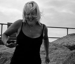 Cheerful mature woman standing at beach against sky