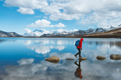 Hiker walking on rocks in lake against sky