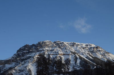 Low angle view of snowcapped mountains against clear blue sky