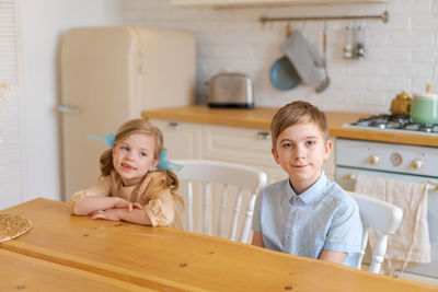 Children sit at table in kitchen and wait for their parents to make them