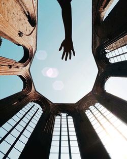 Cropped image of silhouette hand by historic built structure against clear sky