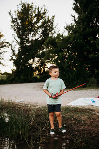 Young boy standing outside at lake holding fishing pole