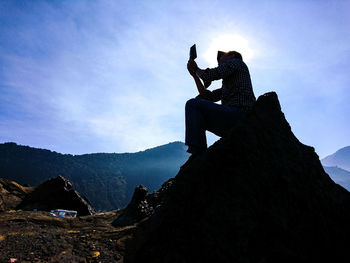 Man sitting on rock against mountain range against sky