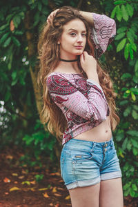 Portrait of beautiful young woman standing against trees