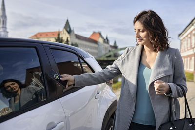 Woman unlocking electric car through smart phone on sunny day