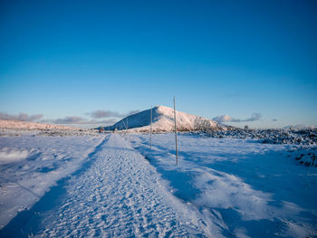 Snow covered land against clear blue sky