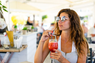 Young woman wearing sunglasses while holding drink in glass