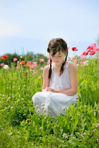 Sad girl sitting amidst plants on field against sky