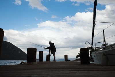 Man fishing on pier over sea against sky