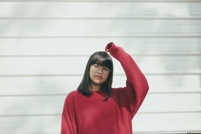 Asian teenager wearing red sweater standing against white wall