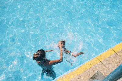 Woman helping her child to jump into the pool