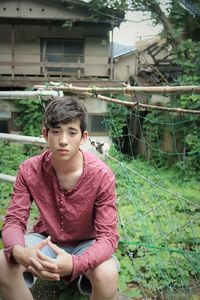 Portrait of young sitting outdoors by derelict country home