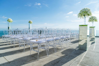 Empty chairs and tables by sea against sky