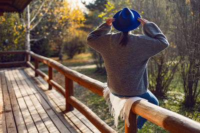 Village woman in a blue hat sits rear at a wooden house in autumn