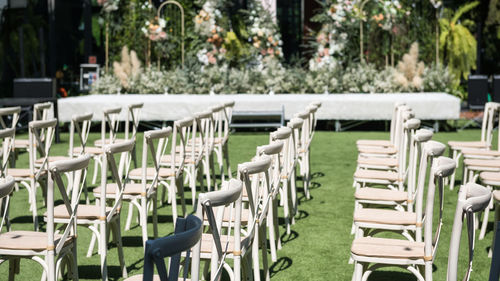 Chairs decorated with flowers in outdoor wedding ceremony in garden.