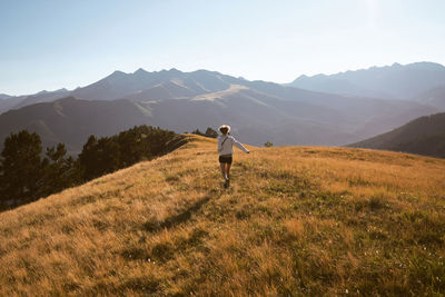 Rear view of man standing on field against mountains