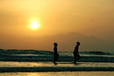 Silhouette couple standing on beach against sky during sunset