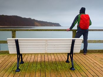 Man in trekking suit in harbor in dark rainy day. touristic mole, wet wooden floor above sea.