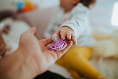 Cropped hand of man giving pacifier to baby girl at home