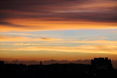 Silhouette cityscape against orange sky