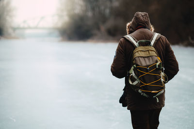 Rear view of man in warm clothes with backpack walking on snowfield