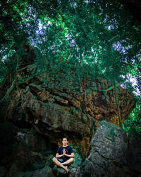 Woman sitting on rock by trees