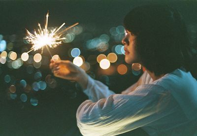 Young woman holding sparkler at night