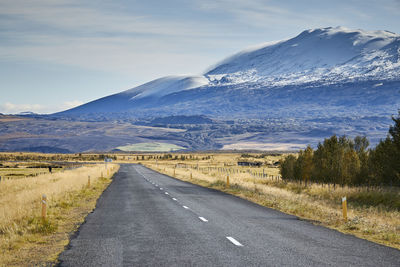 Empty road leading towards mountains against sky