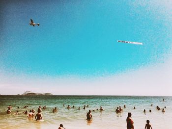 People on beach against clear blue sky