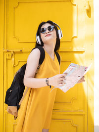 Young woman wearing sunglasses standing against yellow wall