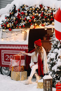 A beautiful young woman with red lips in warm hat stands by a decorated christmas van on the street