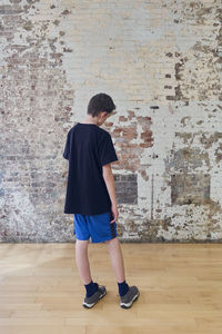 Rear view of boy standing on floor against wall