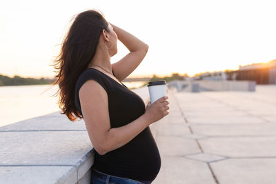 Side view of young woman standing against sky during sunset