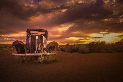 Abandoned truck on field against sky during sunset