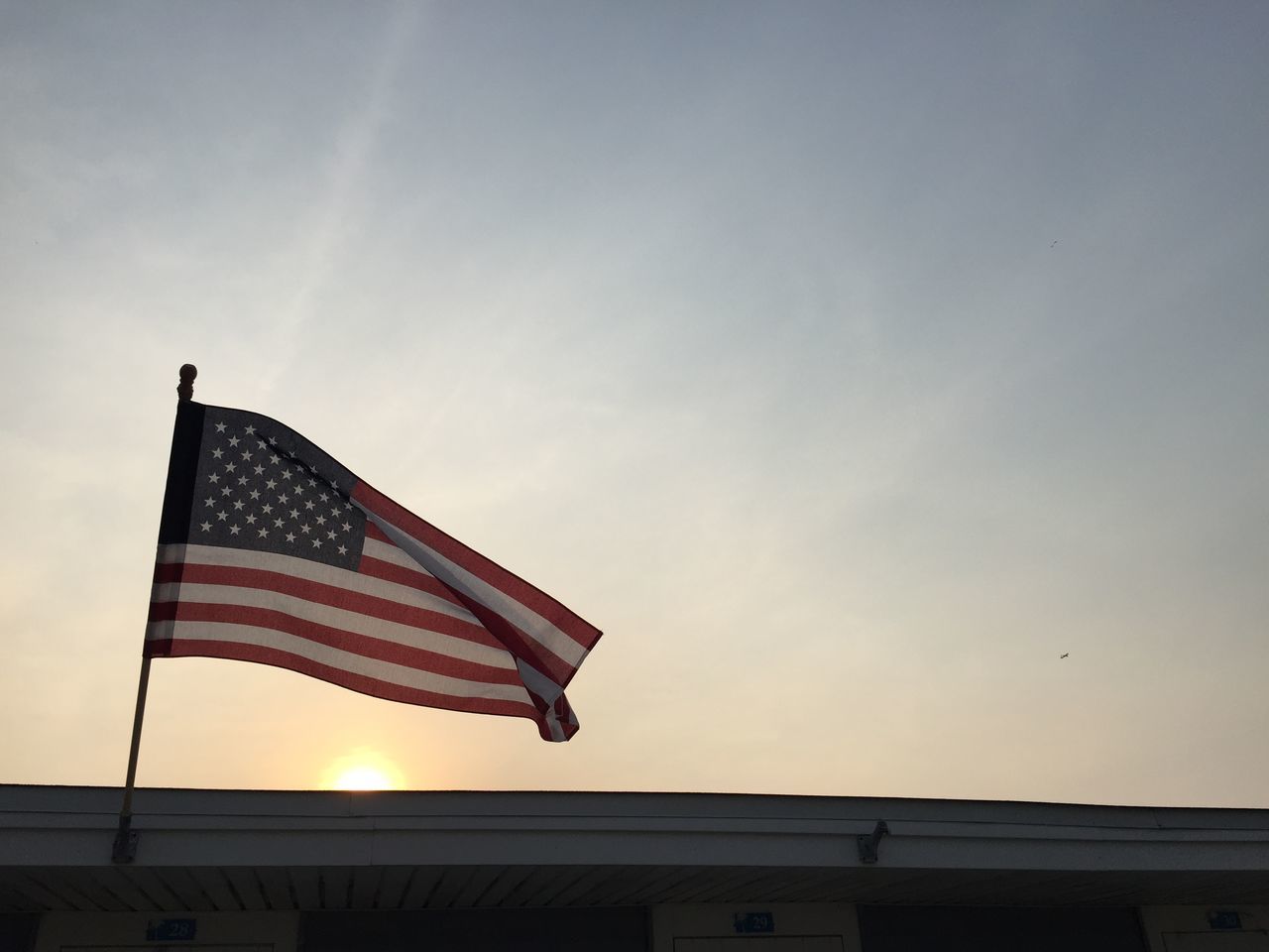 flag, low angle view, identity, patriotism, national flag, sky, american flag, building exterior, built structure, architecture, wind, striped, no people, outdoors, cloud, culture, cloud - sky, sunlight, day, copy space